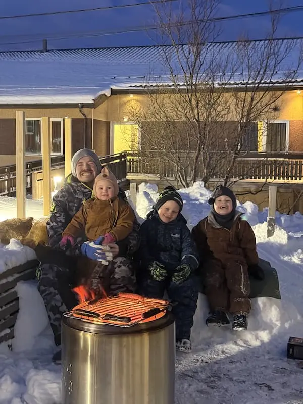 Smilende barn og voksen som sitter ute i snøen
